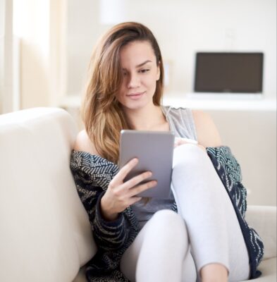 young woman sitting on a couch searching for answers on her ipad